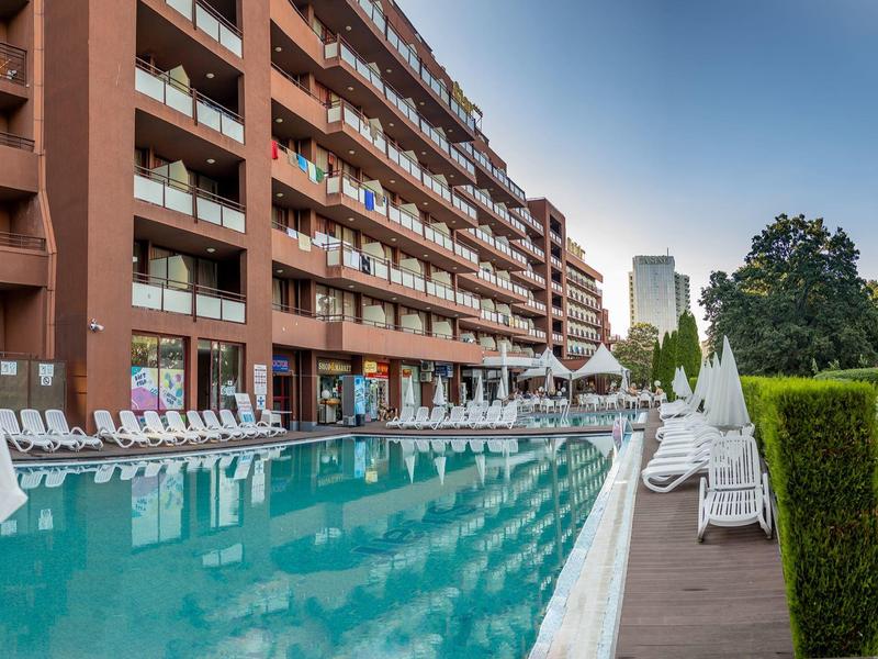 Großer Außenpool neben einem mehrstöckigen Hotelgebäude mit Sonnenliegen und Schirmen im Freien.