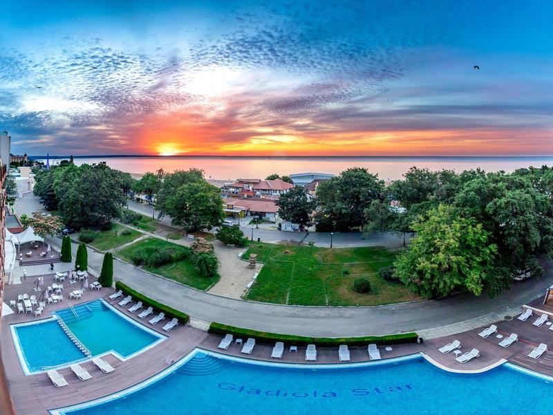 Blick auf einen Pool mit Liegestühlen und einen Park bei Sonnenuntergang in der Nähe eines Hotels.