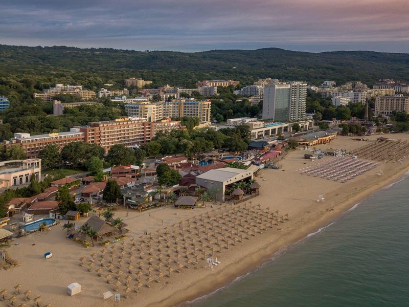 Strand mit Reihen von Sonnenschirmen und Hotels im Hintergrund bei bewölktem Himmel.