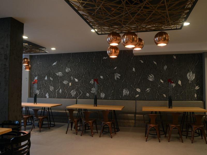 Moderne Hotelbar mit dunkler Wandgestaltung, Holztischen und Stuhlreihen unter warmen Pendelleuchten.