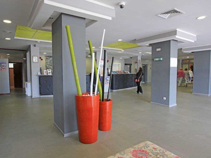 Heller Empfangsbereich mit grauen Säulen, rotem Deko-Behälter und modernem Design.