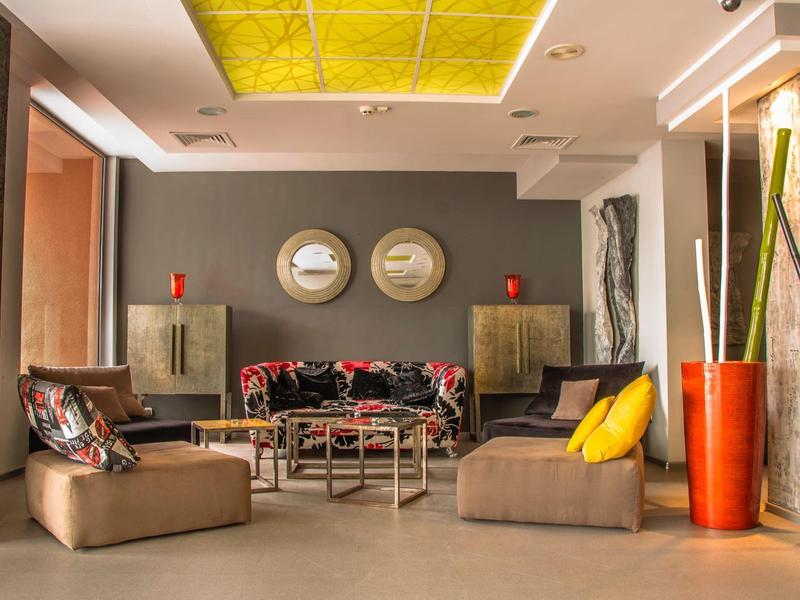 Modernes Wohnzimmer mit beiger Couch, bunten Kissen, grauer Wand und zwei runden Spiegeln sowie orangen Vasen.