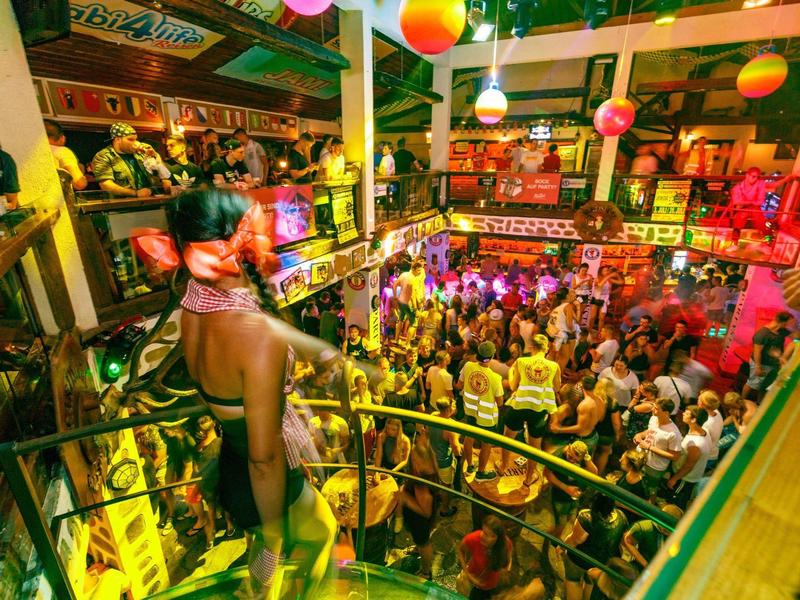 Bunte, volle Party mit tanzenden Menschen und lebhafter Beleuchtung in mehrstöckigem Club.