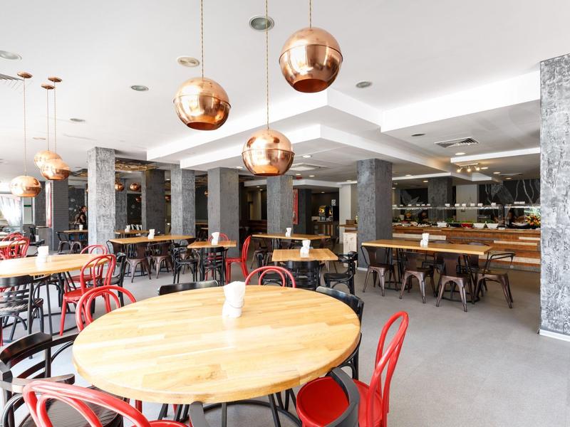 Großer moderner Gastraum mit runden Holztischen, roten Stühlen und kupferfarbenen Pendelleuchten.