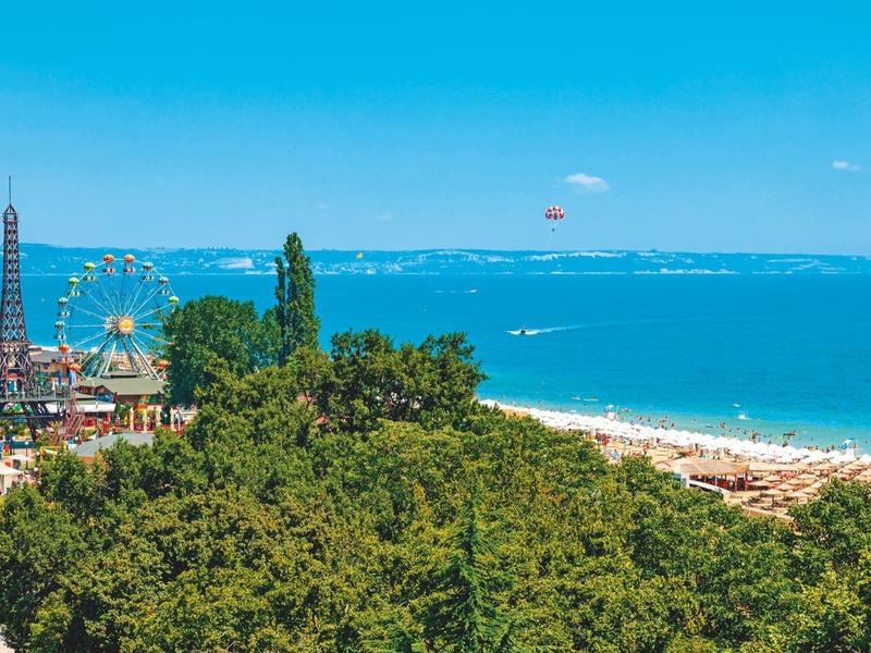 Küste mit Strand, Bäumen, Riesenrad, Eiffelturm-Nachbildung und klarem blauem Himmel.