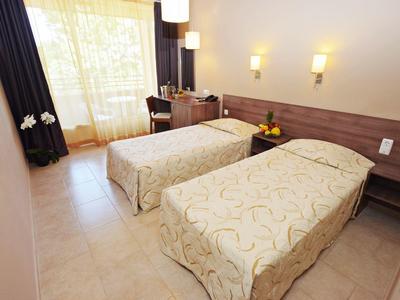 Lichte hotelkamer met twee eenpersoonsbedden, bureau en groot raam met gordijnen.