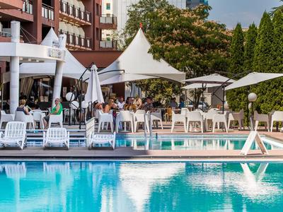 Hotelpoolbereich mit Liegestühlen, Sonnenschirmen und Gästen im Freien bei sonnigem Wetter
