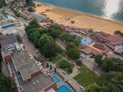 Luchtfoto van een hotel met zwembad, groene bomen en strand met parasols aan zee
