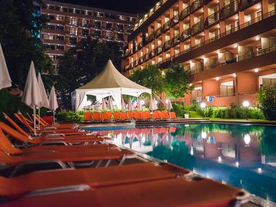 Beleuchteter Hotelpool mit Liegestühlen und Sonnenschirmen in der Nacht.