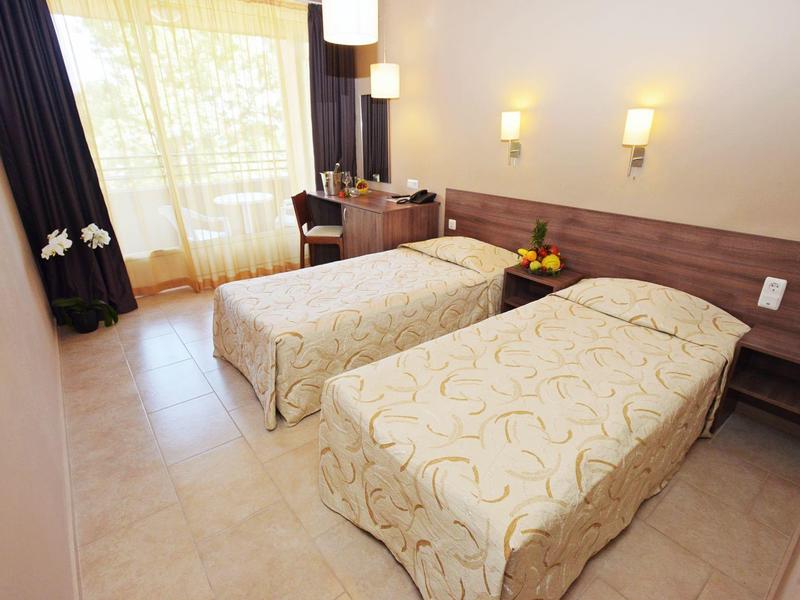 Lichte hotelkamer met twee eenpersoonsbedden, bureau en groot raam met gordijnen.