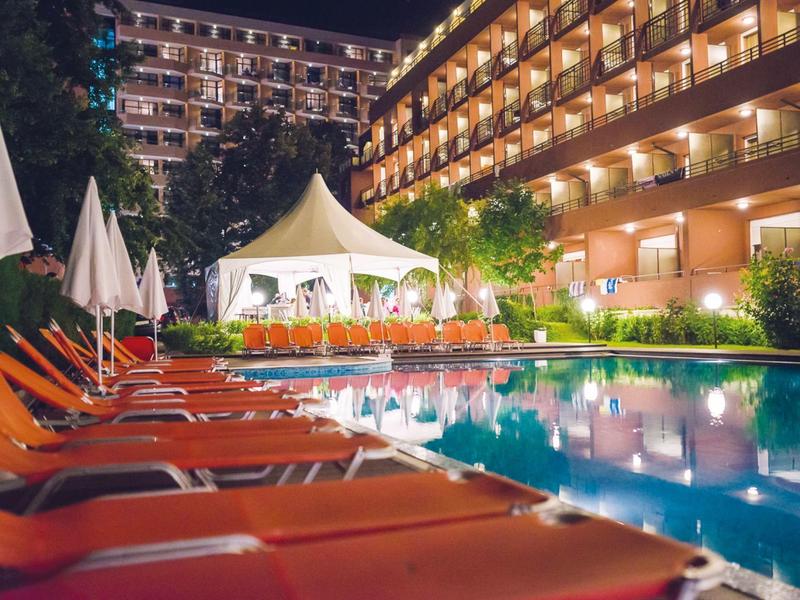 Verlicht hotelzwembad met ligstoelen en parasols ’s nachts.