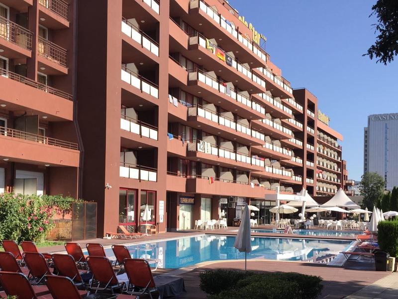 Groot hotelgebouw met meerdere balkons en een zwembad met ligstoelen en parasols.