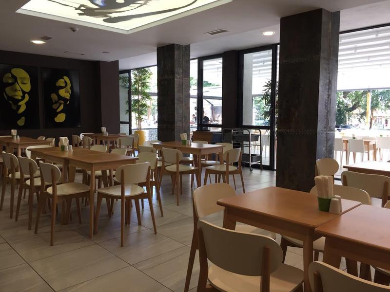 Modern restaurant met houten tafels en stoelen, grote ramen en minimalistische inrichting.