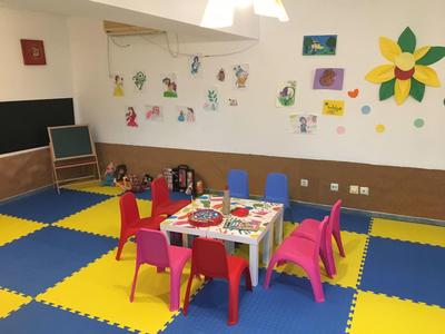 Bunter Kinderspielraum mit kleinen Stühlen, Tischen, Wanddekorationen und Spielecke auf buntem Boden.