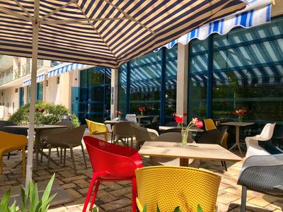 Sonniger Außensitzbereich mit bunten Stühlen und Tischen unter dunkel gestreiften Markisen.