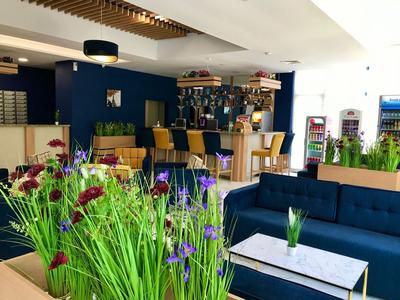 Moderner Hotel-Loungebereich mit Bar, blauen Sitzmöbeln und frischen Blumen auf Tischen.