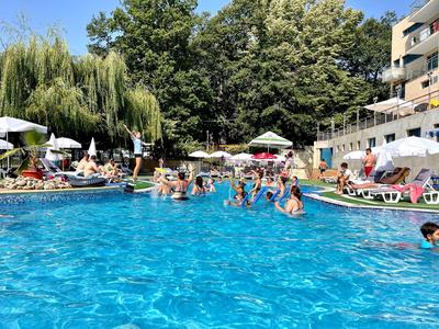 Menschen entspannen und schwimmen in einem großen Pool mit Sonnenschirmen und Bäumen im Hintergrund.