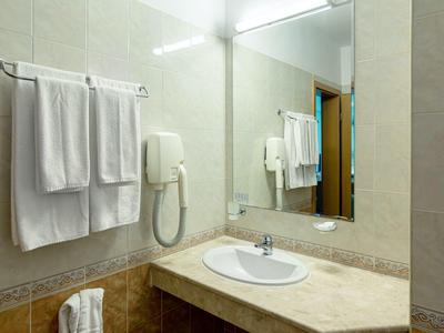 Heller Badbereich mit weißem Waschbecken, großem Spiegel, Handtüchern und Wandfön.