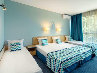 Hellblau gestrichenes Schlafzimmer mit drei Betten, gemusterten Bettdecken und großen dunkelblauen Vorhängen.