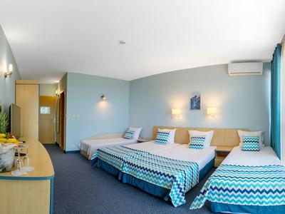 Hell eingerichtetes Hotelzimmer mit drei Betten, blauen Wänden und Teppichboden.