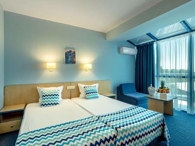 Modernes Hotelzimmer mit zwei Einzelbetten, blauen Akzenten und großem Fenster mit Vorhängen.