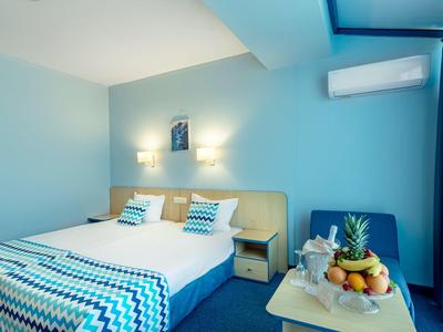 Modernes Schlafzimmer mit großem Bett, blauem Wandanstrich, Nachttischen und Obstkorb auf Tisch.