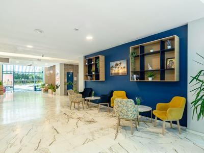 Moderner Hotel-Loungebereich mit Marmorfliesen, Sitzgelegenheiten und blauer Wand mit Regalen.