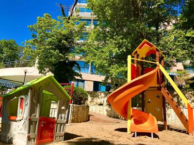Bunter Kinderspielplatz mit Spielhaus und rutschiger Rutsche vor grünem Bewuchs und blauem Himmel.