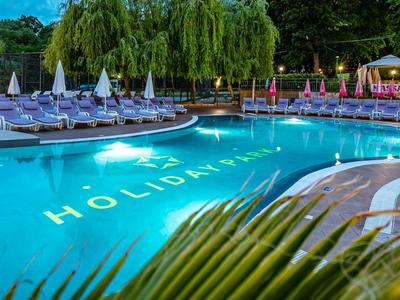 Beleuchteter Hotel-Pool mit Liegestühlen und Palmen bei Dämmerung