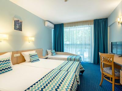 Ein helles Hotelzimmer mit zwei Betten, blauen Vorhängen, Teppich und Holzmöbeln.