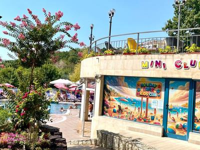 Außenansicht eines Hotels mit einem Miniclub, umgeben von Blumen und Sonnenschirmen.