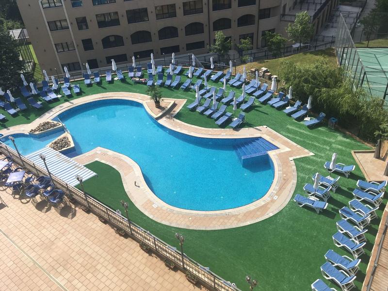 Außenpool mit unregelmäßiger Form, umgeben von blauen Liegestühlen auf grüner Rasenfläche.