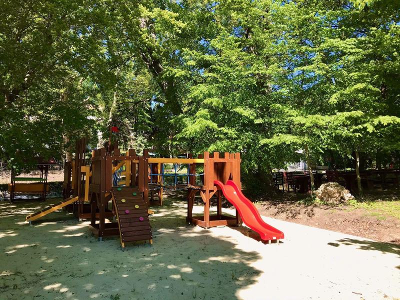 Kinderspielplatz mit Klettergerüst, roter Rutsche und vielen grünen Bäumen im Hintergrund.