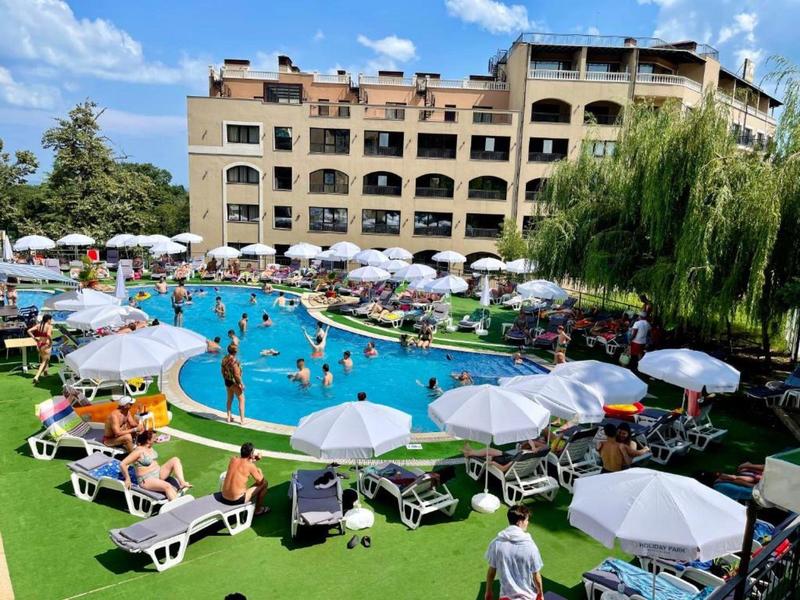 Großer blauer Pool mit Liegestühlen, Sonnenschirmen und einem mehrstöckigen Gebäude im Hintergrund.