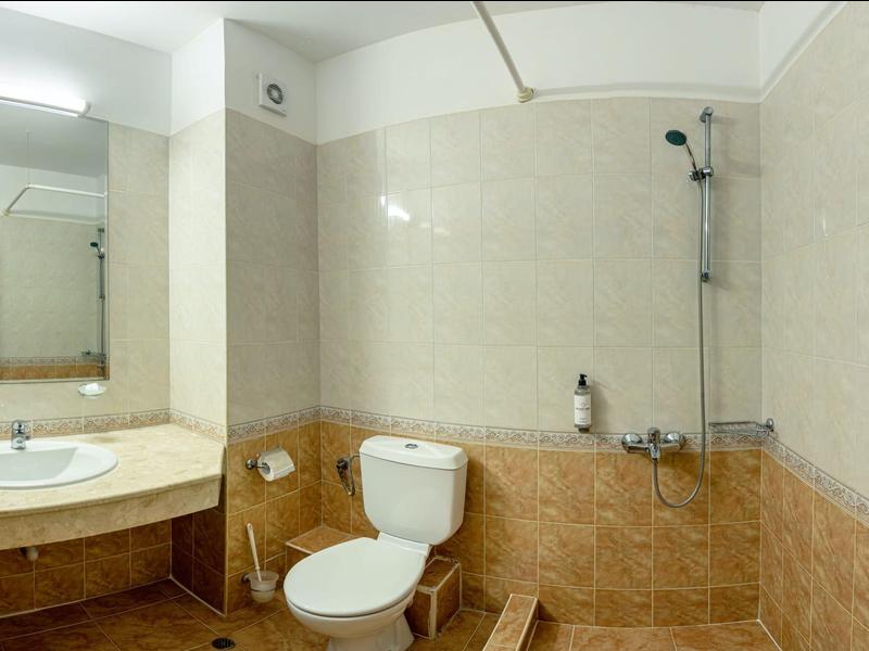 Modernes Badezimmer mit weißen und beigen Fliesen, Toilette, Waschbecken und Duschwanne mit Glasabtrennung.