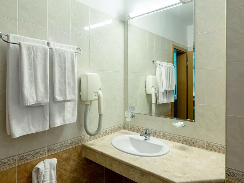 Heller Badbereich mit weißem Waschbecken, großem Spiegel, Handtüchern und Wandfön.