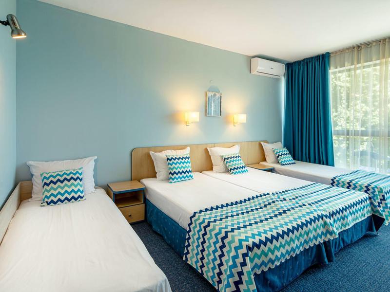 Hellblau gestrichenes Schlafzimmer mit drei Betten, gemusterten Bettdecken und großen dunkelblauen Vorhängen.