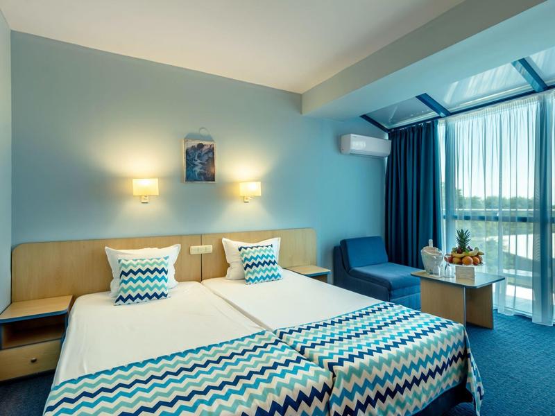 Modernes Hotelzimmer mit zwei Einzelbetten, blauen Akzenten und großem Fenster mit Vorhängen.