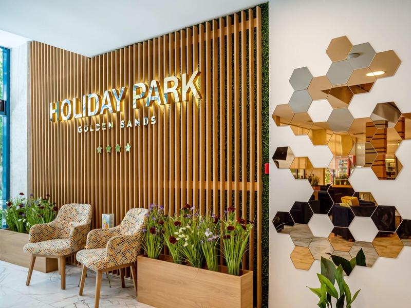 Moderne Lobby mit Holzvertäfelung, zwei Sesseln, Pflanzen und Waben-Spiegelgestaltung.