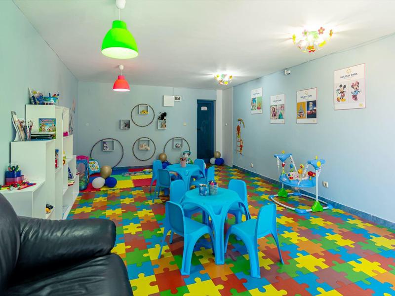Bunter Spielraum mit Puzzlematten, blauen Kindertischen, Fahrrädern und Schaukeln an der Wand.