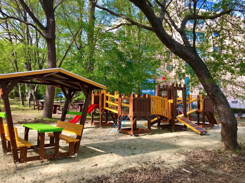 Bunter Spielplatz mit Rutschen, Klettergerüst und Holztisch mit Bank unter Bäumen.