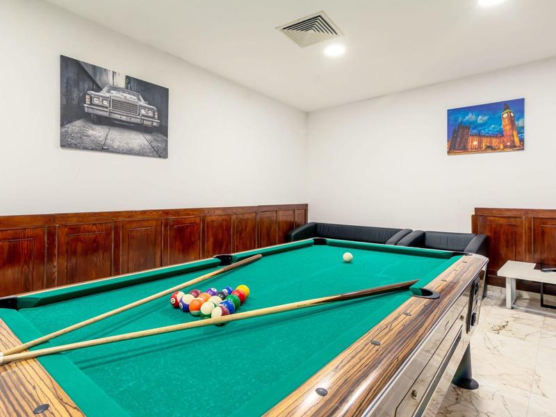 Billardtisch mit grünem Filz, zwei Queue-Stöcken, Bällen und weißen Wänden mit Bildern.