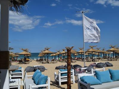 Hotel de playa con área de descanso, sombrillas y vista al mar azul bajo un cielo despejado.