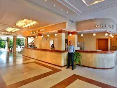 Lobby de hotel amplia y luminosa con recepción, gran candelabro y elementos decorativos.