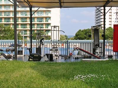 Zona de gimnasio al aire libre con equipos junto a un lago, rodeada de edificios residenciales.