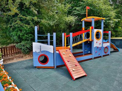 Barco de juegos de madera colorido en un área pavimentada dentro de un bosque