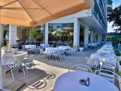 Terraza de hotel con mesas y sillas blancas bajo una gran sombrilla.