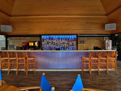 Área de bar moderna con filas de sillas de madera e iluminación LED azul en el interior.