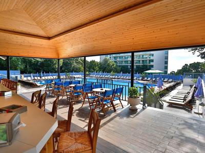 Terraza cubierta con mesas y sillas junto a piscina con tumbonas y sombrillas azules.