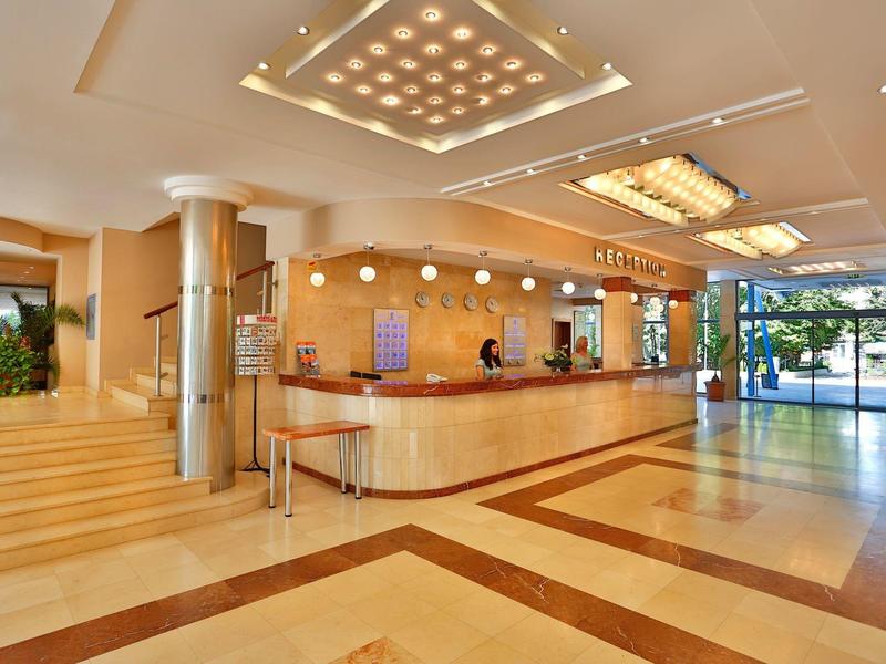 Amplio vestíbulo de hotel con recepción, suelo de mármol y iluminación moderna a plena luz del día.